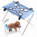 Blue mesh pet grooming hammock stand with eight black-edged openings and a silver folding frame, featuring an inset image of a small dog using a similar stand.