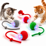 Multiple interactive cat toy balls with LED lights and rope tails arranged on a clean white background, with gray and orange tabby cats investigating the toys.