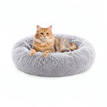 Round grey plush pet bed with an orange tabby cat resting inside.

