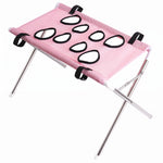 Pink mesh pet grooming hammock stand with black-edged openings, black straps, silver folding frame, and white foot caps on a white background.
